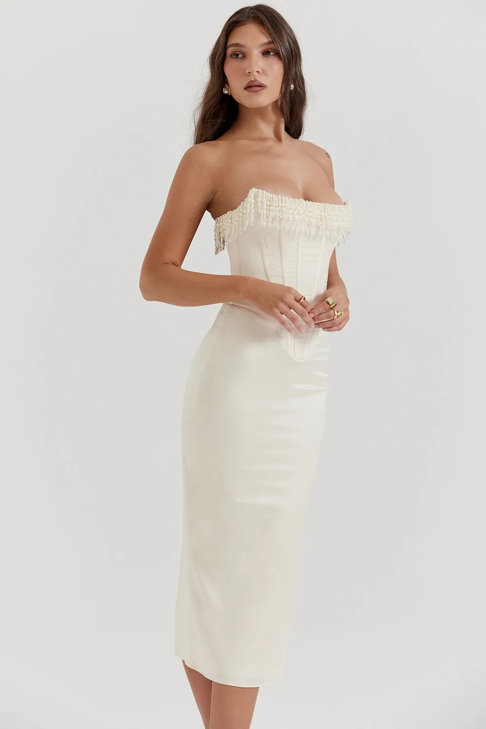 Modelo usando vestido midi blanco sin tirantes con detalle de perlas en el busto. Corte elegante ideal para boda civil o eventos formales.
