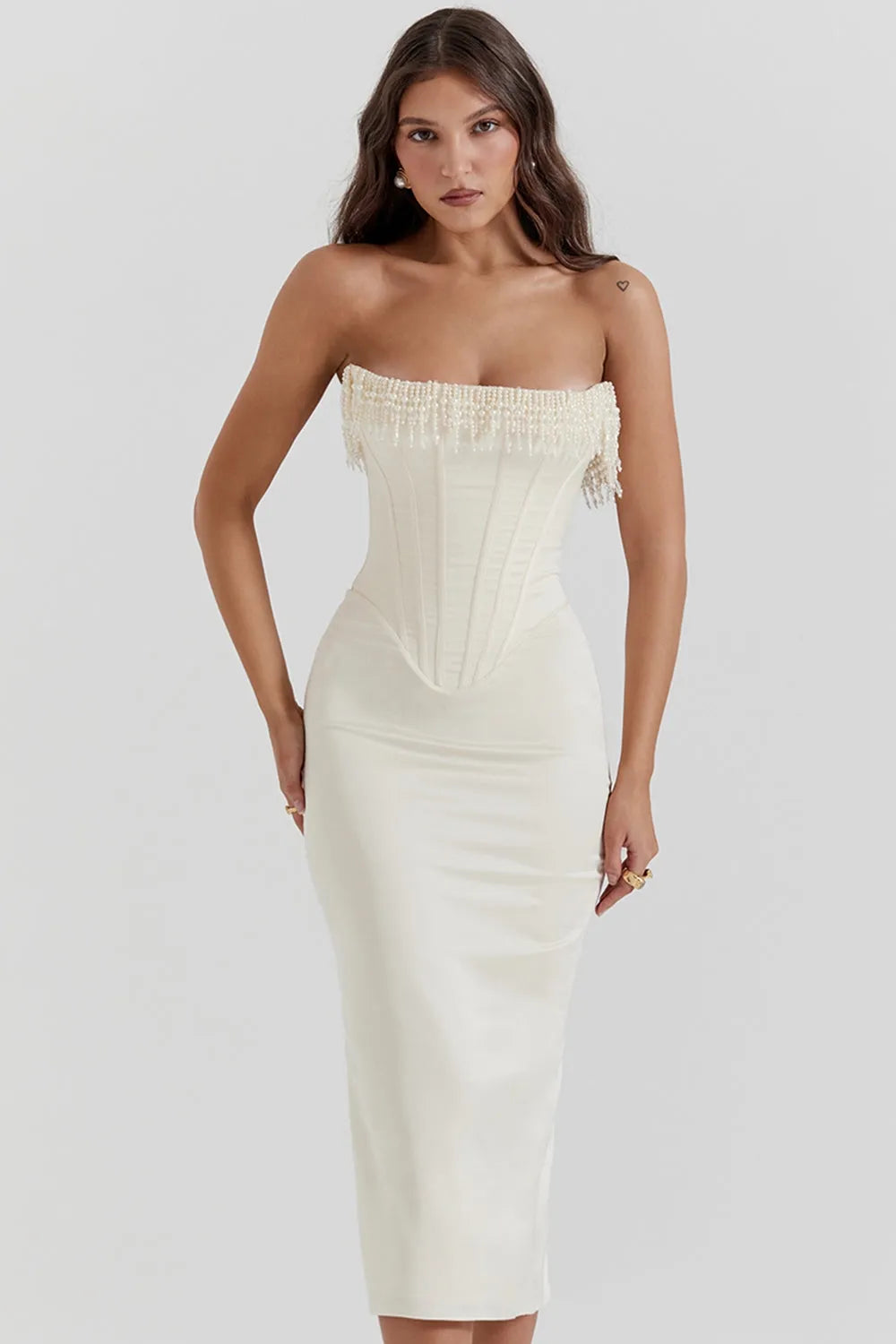 Modelo usando vestido midi blanco sin tirantes con detalle de perlas en el busto. Corte elegante ideal para boda civil o eventos formales.

