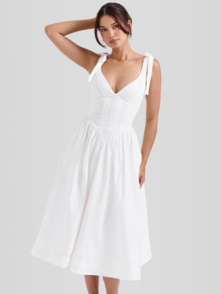 Modelo usando vestido midi blanco sin mangas con corset estructurado y ballenas internas. Diseño elegante con bolsillos discretos y ajuste entallado.
