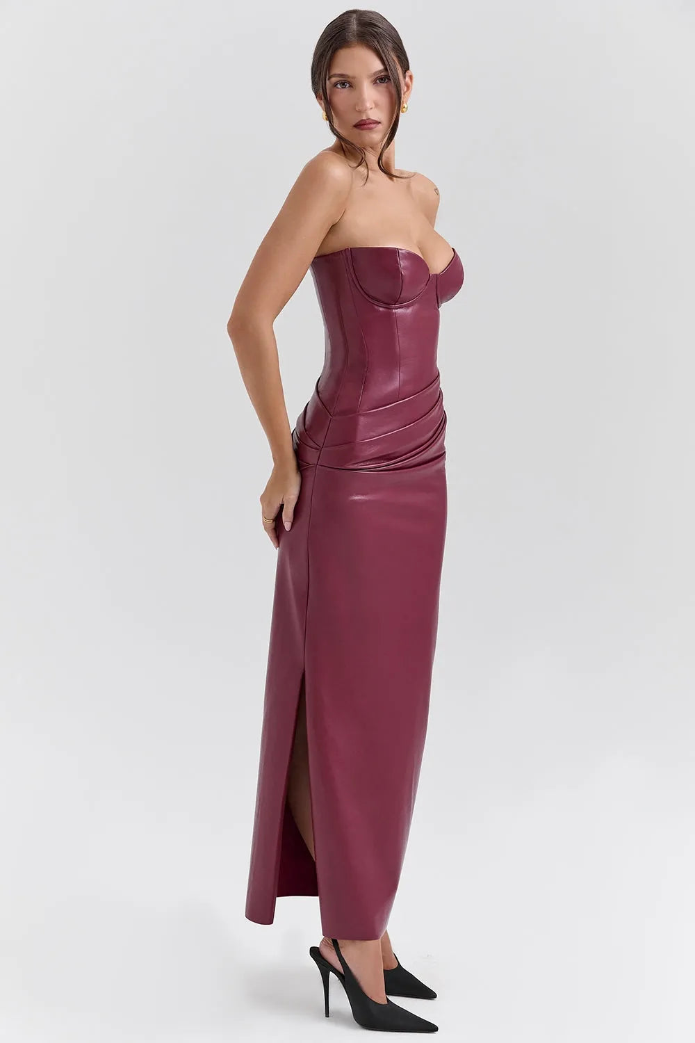 Mujer usando un vestido largo elegante en cuero vegano color vino, con corset estructurado sin tirantes y abertura lateral, ideal para gala o eventos de noche.